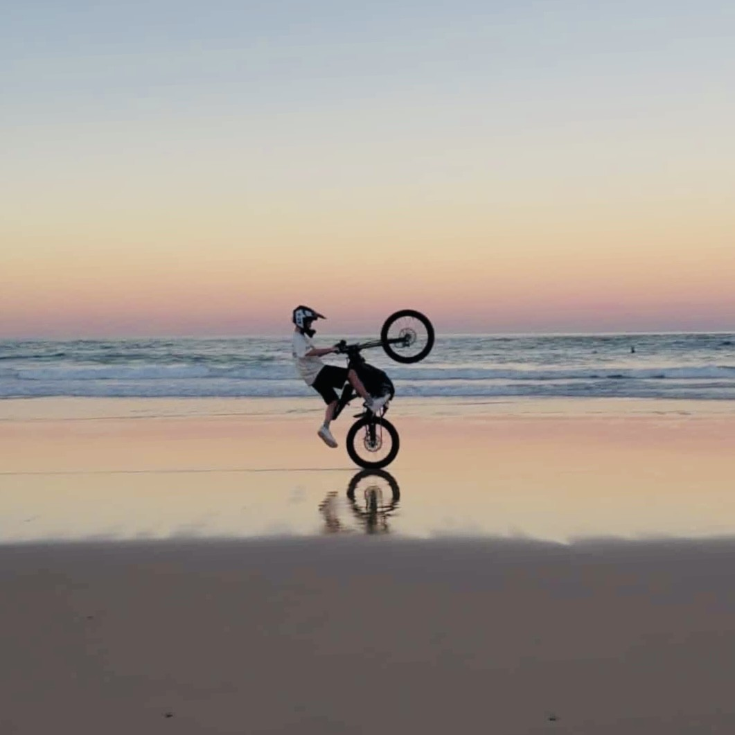 Person performing a bike trick on a beach at sunset